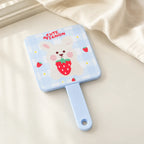Blauer MUMUSO Handspiegel mit Hasenmotiv und Erdbeeren auf heller Ablage