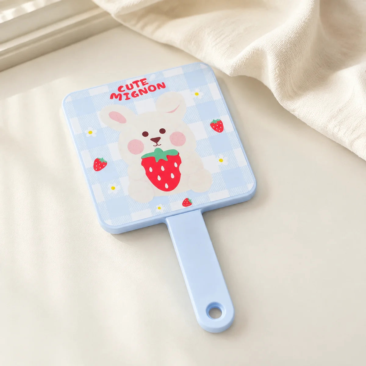 Blauer MUMUSO Handspiegel mit Hasenmotiv und Erdbeeren auf heller Ablage